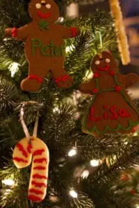 Homemade gingerbread and candy cane ornaments hanging on a decorated Christmas tree with lights