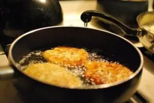 Golden potato pancakes frying in oil in a black skillet on stovetop