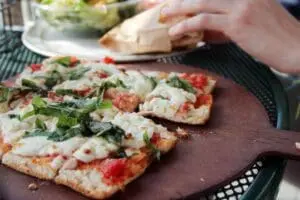 Sliced flatbread pizza topped with cheese, tomato sauce, and fresh arugula on a wooden board