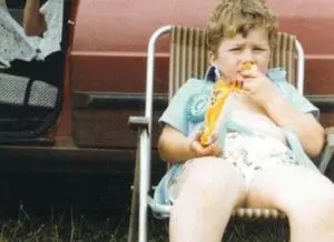 Young child eating a hot dog outdoors near an RV