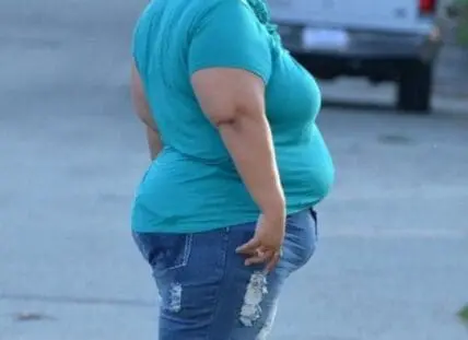 Person with obesity standing outdoors wearing a turquoise shirt and jeans
