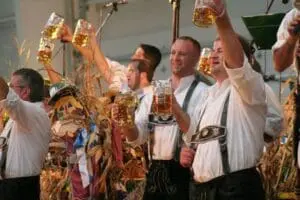 Men in traditional Bavarian clothing toasting with beer glasses and wheat sheaves at Oktoberfest