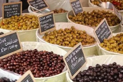 Various olive varieties displayed in white containers at a market stall with small chalkboard price