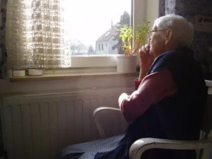 Elderly man gazing out window while sitting indoors