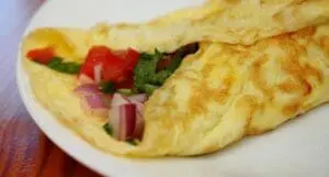 Fluffy omelet filled with diced tomatoes and green onions on a white plate