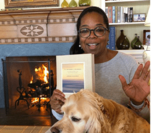 Woman holding a book by a fireplace with a golden retriever