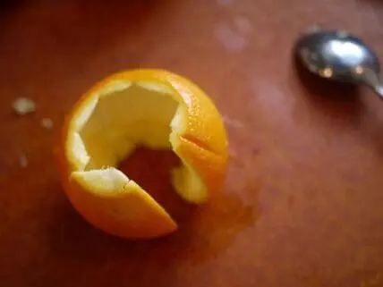 Freshly peeled orange with spiral peel and spoon on wooden surface