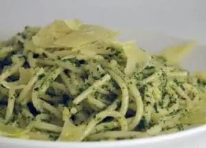 Plate of spaghetti coated with green basil and arugula pesto