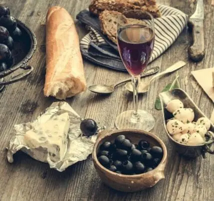 Image of glass of red wine next to baguette, cheese, olives and more. Amazing Organic Red Wines are delicious!