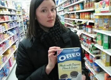 Woman holding a box of Oreo cookies in a grocery store aisle