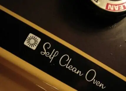 Close-up of an oven door showing "Self Clean Oven" text and icon on black and gold trim