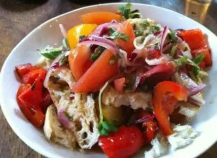 Rustic salad with torn bread, roasted red peppers, red onions, and fresh herbs on white plate
