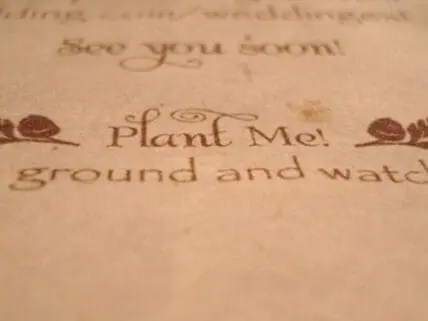 Close-up of plantable seed paper invitation with text "Plant Me!" and decorative floral elements
