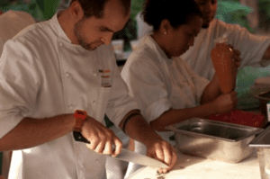 Two chefs in white coats preparing food at an outdoor cooking demonstration.