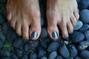 Bare feet with metallic nail polish on dark river stones