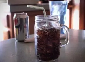 Glass of cola with ice and straw next to a soda can