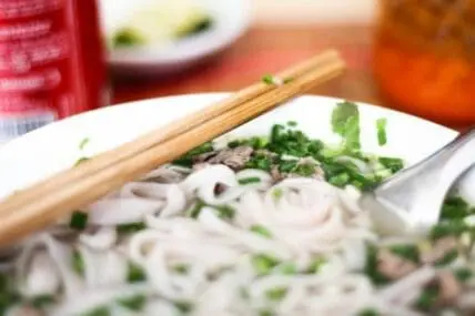 Bowl of rice noodles with green onions and chopsticks