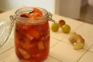Jar of homemade pickled vegetables with fresh ginger and grapes on wooden surface