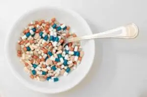Colorful pharmaceutical capsules and pills in a white bowl with a spoon