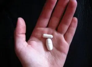 Two white pills arranged on an open palm against a dark background