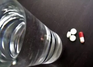 Overturned glass jar with white tablets and red-and-white capsule on dark surface