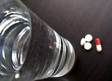 Overturned glass jar with white tablets and red-and-white capsule on dark surface