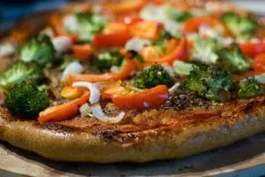 Vegetable pizza with broccoli, red peppers, and onions on a wooden surface