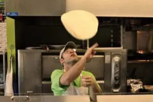 Man in green shirt tossing pizza dough in a kitchen