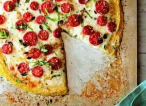 Gluten-free polenta pizza topped with tomatoes, cheese, and fresh herbs on parchment paper