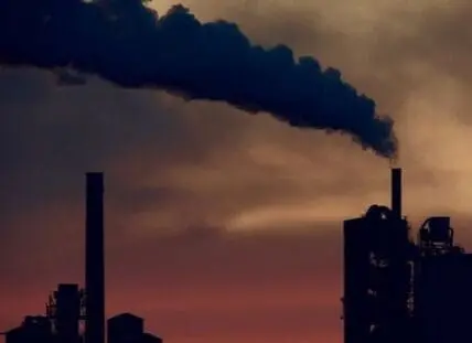 Industrial factory silhouette with dark smoke plume against sunset sky