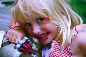 Young child with blonde hair holding a red popsicle and smiling