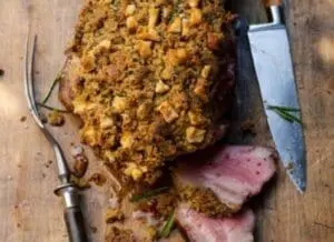 Sliced pork roast with golden mustard and herb crust on wooden cutting board