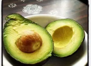 Two avocado halves with pits on a decorative plate