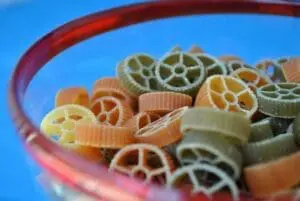 Colorful wheel-shaped pasta in a pink bowl against a blue background
