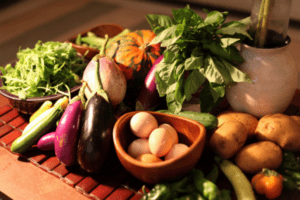Fresh produce including vegetables, herbs, eggs, and potatoes arranged on a terracotta surface