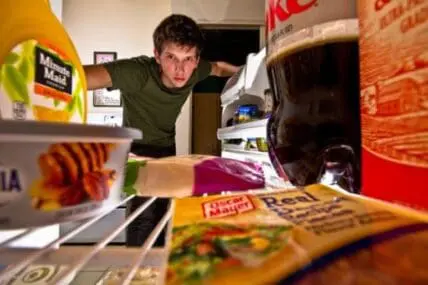 Man looking into an open refrigerator filled with food items and containers