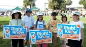 Group of six people holding "Yes on 37" signs at an outdoor event supporting GMO labeling