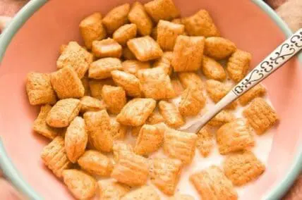 Bowl of cinnamon square cereal pieces in milk with spoon