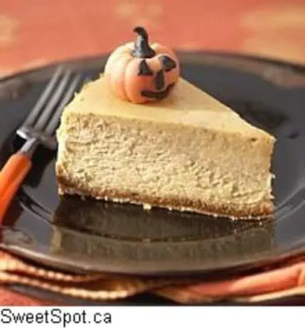 Pumpkin cheesecake slice with jack-o'-lantern decoration on dark plate