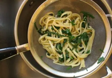 image of pasta and greens in a colandar in a large pot in a sink