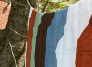 Colorful handmade patchwork quilt with striped fabric panels hanging on a clothesline outdoors