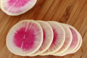 Sliced watermelon radishes showing pink and white flesh on wooden surface