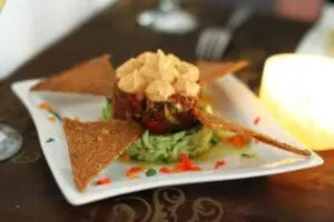 Plated dish with seared red meat patty topped with cauliflower puree, served with avocado mousse