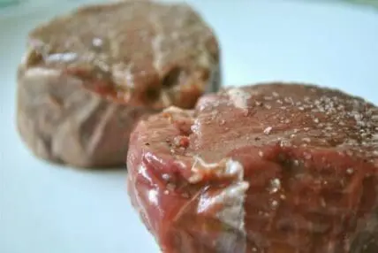Two raw steaks with salt crystals on white surface