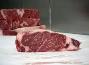 Raw steaks with marbling displayed on white surface