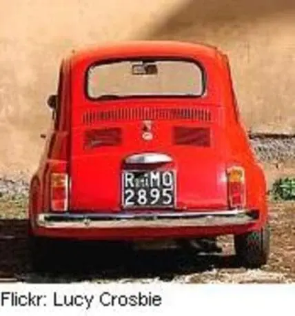 Rear view of a red vintage Fiat 500 parked against a weathered wall