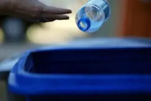 Hand dropping plastic bottle into blue recycling bin