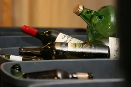 Wine bottles and a green glass bottle lying in a recycling bin