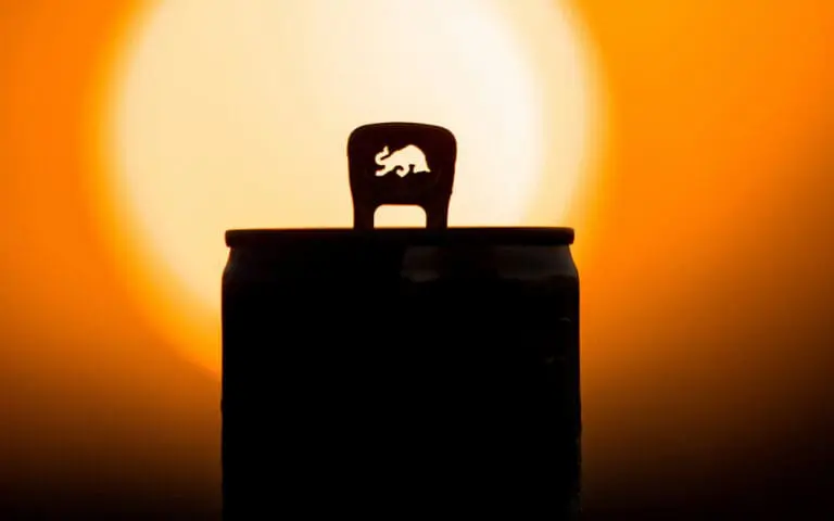 image of the top of a Red Bull can and it's pull tab on orange background that looks like a sunset.