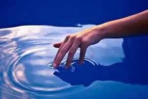 Hand touching water surface creating ripples in blue pool